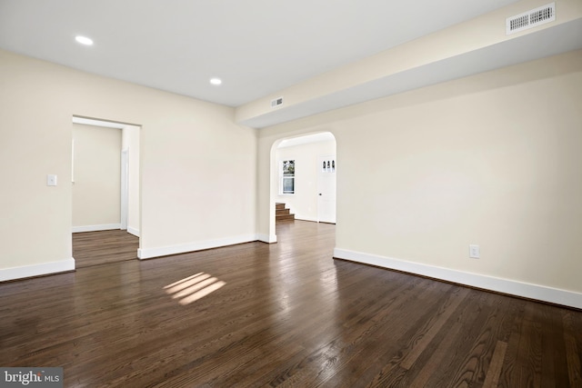 unfurnished room with visible vents, arched walkways, baseboards, and dark wood-style flooring