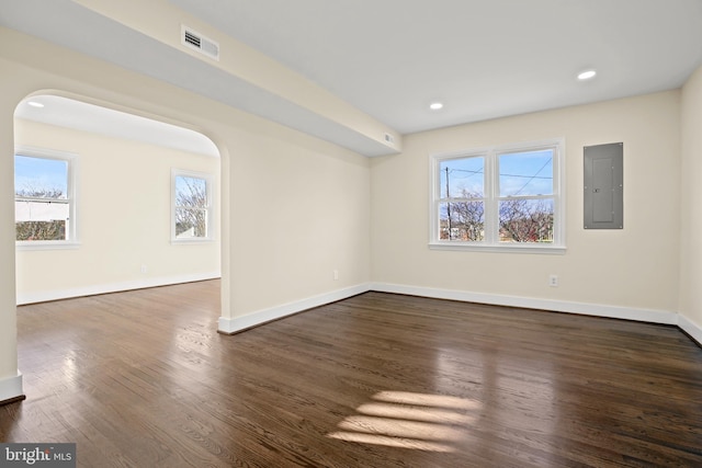 unfurnished room featuring visible vents, electric panel, wood finished floors, arched walkways, and baseboards