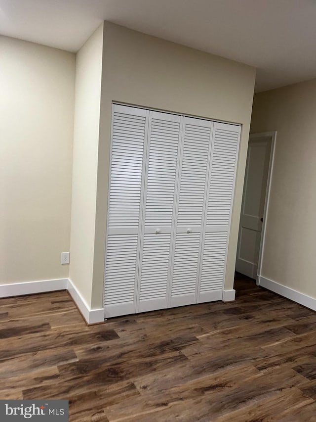 unfurnished bedroom with dark wood-style floors, a closet, and baseboards