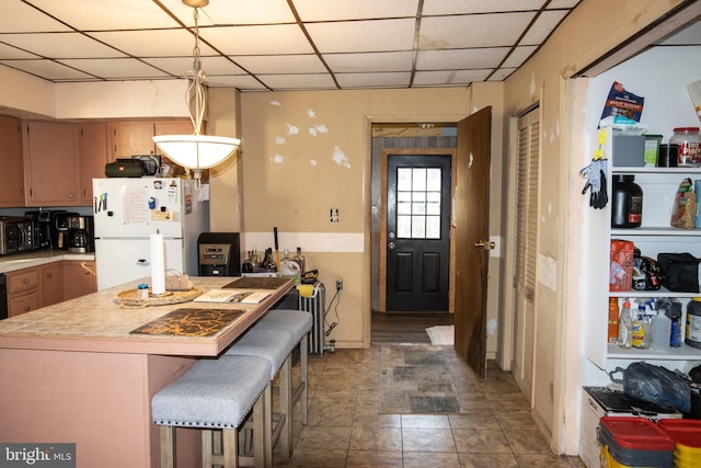 kitchen with a paneled ceiling, decorative light fixtures, white fridge, and a kitchen bar