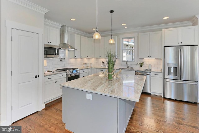 kitchen with appliances with stainless steel finishes, sink, wall chimney range hood, a center island, and white cabinetry