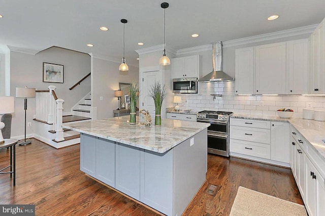 kitchen with wall chimney range hood, a kitchen island, dark hardwood / wood-style flooring, white cabinets, and appliances with stainless steel finishes