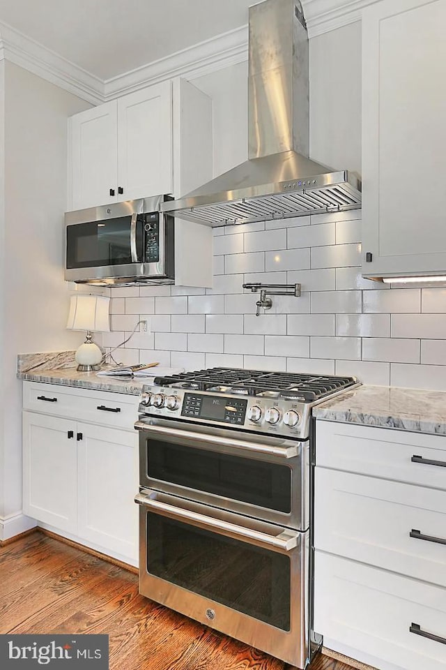 kitchen with white cabinets, stainless steel appliances, hardwood / wood-style flooring, and wall chimney range hood