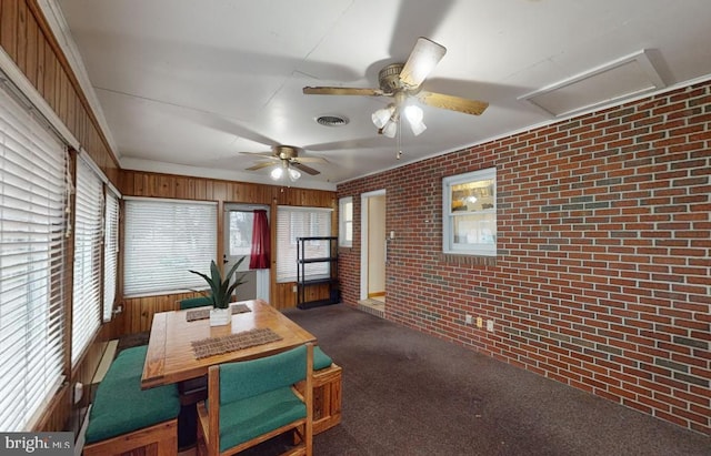 carpeted dining room with a wealth of natural light, wood walls, and brick wall