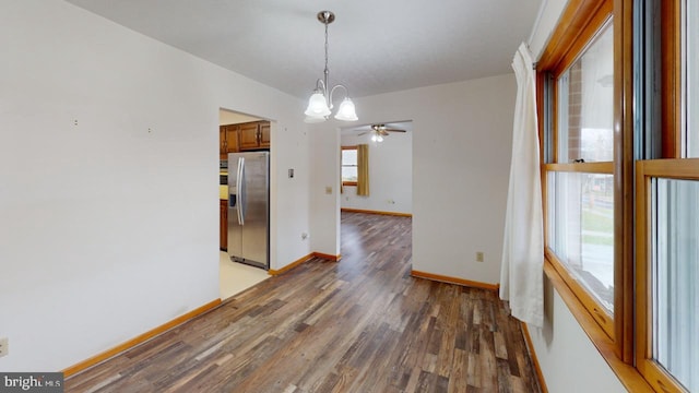 unfurnished dining area featuring ceiling fan with notable chandelier and dark hardwood / wood-style flooring