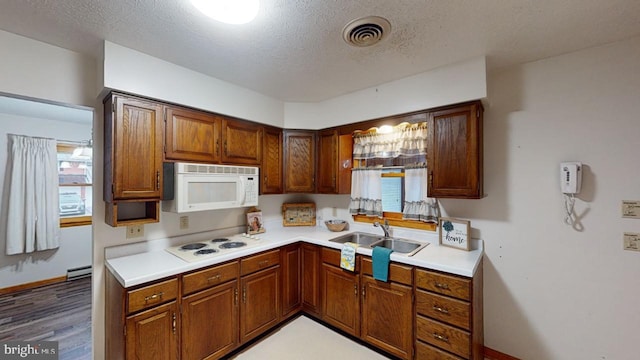 kitchen with a textured ceiling, white appliances, baseboard heating, sink, and dark hardwood / wood-style floors