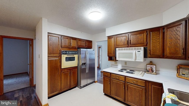 kitchen with a textured ceiling, white appliances, and light hardwood / wood-style flooring