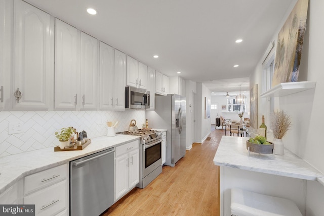 kitchen with light stone countertops, stainless steel appliances, white cabinetry, and light hardwood / wood-style floors