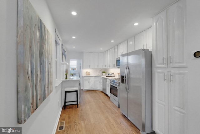 kitchen with a breakfast bar area, light hardwood / wood-style flooring, white cabinets, and stainless steel appliances