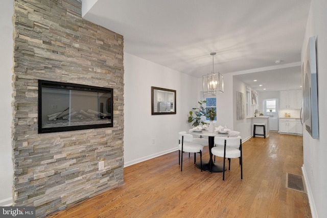 dining area featuring light wood-type flooring, a fireplace, and a chandelier