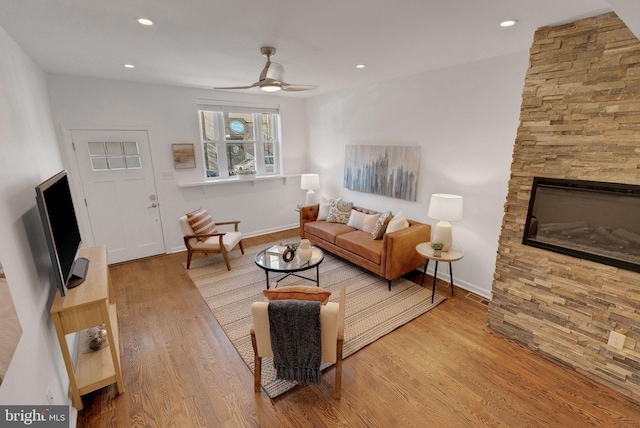 living room with a stone fireplace, ceiling fan, and light hardwood / wood-style flooring