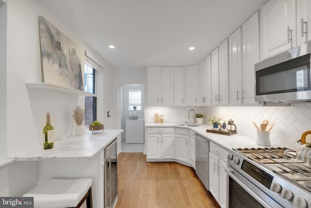 kitchen featuring white cabinets, washer / dryer, stainless steel appliances, and light hardwood / wood-style flooring