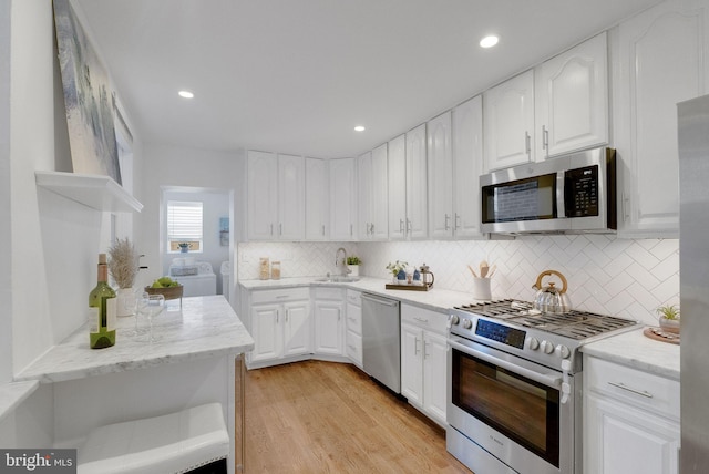 kitchen with sink, light hardwood / wood-style flooring, washer and clothes dryer, white cabinets, and appliances with stainless steel finishes