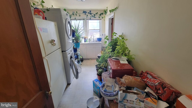 kitchen with light floors, light countertops, white cabinets, stacked washer / drying machine, and a sink