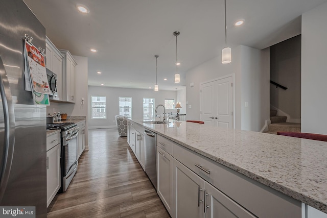 kitchen with light stone countertops, stainless steel appliances, pendant lighting, hardwood / wood-style flooring, and white cabinets