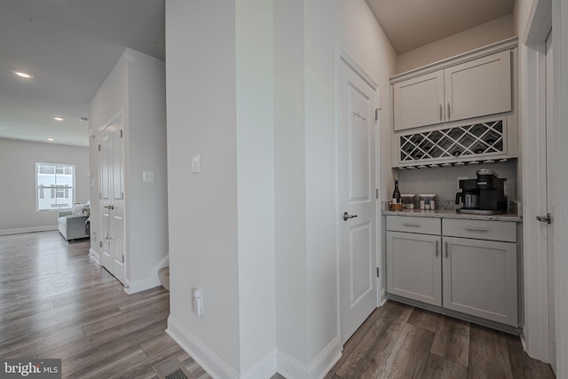 bar featuring light stone countertops, light wood-type flooring, and gray cabinets