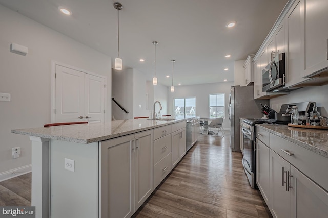 kitchen with appliances with stainless steel finishes, sink, pendant lighting, hardwood / wood-style flooring, and an island with sink