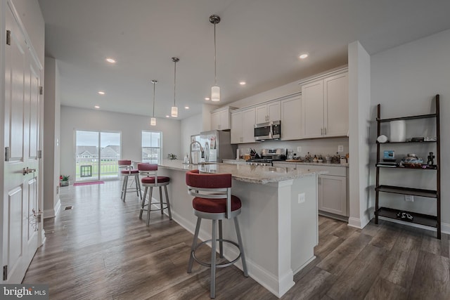 kitchen with stainless steel appliances, dark wood-type flooring, decorative light fixtures, a center island with sink, and white cabinetry