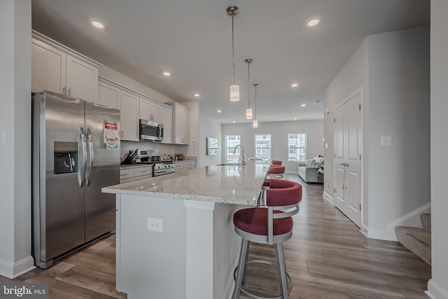 kitchen with a kitchen bar, stainless steel appliances, decorative light fixtures, light hardwood / wood-style flooring, and an island with sink