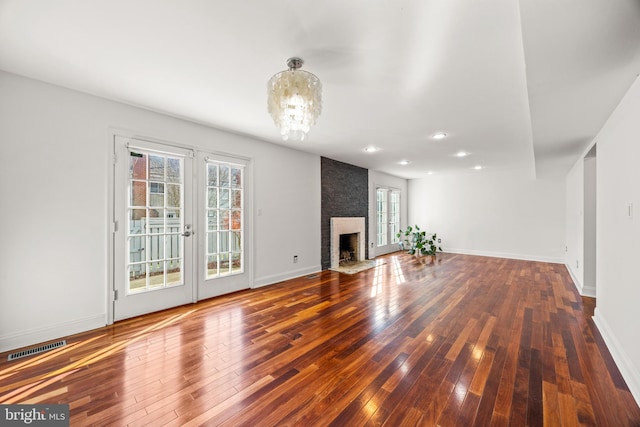 unfurnished living room with hardwood / wood-style flooring, a large fireplace, and a chandelier