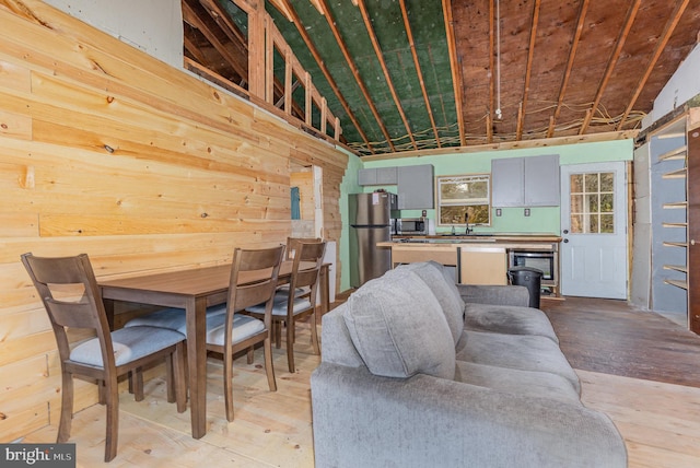 dining area featuring wooden walls, light hardwood / wood-style flooring, lofted ceiling, and sink