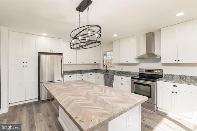 kitchen featuring appliances with stainless steel finishes, wall chimney exhaust hood, white cabinets, hardwood / wood-style floors, and a kitchen island