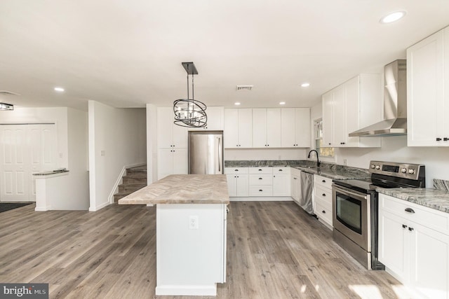 kitchen with wall chimney exhaust hood, a center island, light wood-type flooring, and appliances with stainless steel finishes