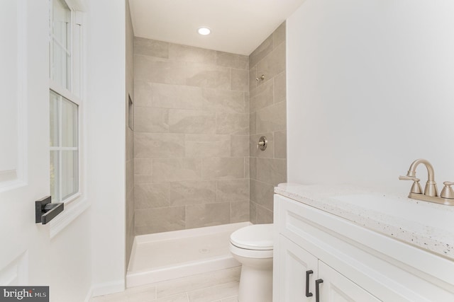 bathroom featuring a tile shower, vanity, and toilet