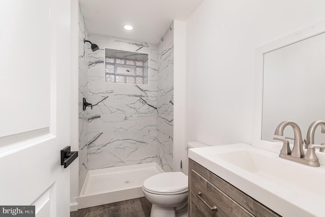 bathroom with a tile shower, vanity, hardwood / wood-style flooring, and toilet