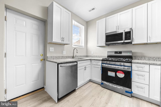 kitchen with sink, white cabinetry, stainless steel appliances, and light wood-type flooring