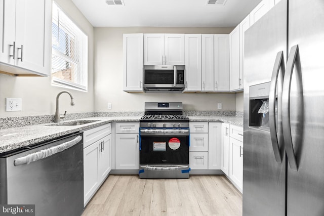 kitchen with light stone countertops, appliances with stainless steel finishes, sink, white cabinets, and light hardwood / wood-style floors