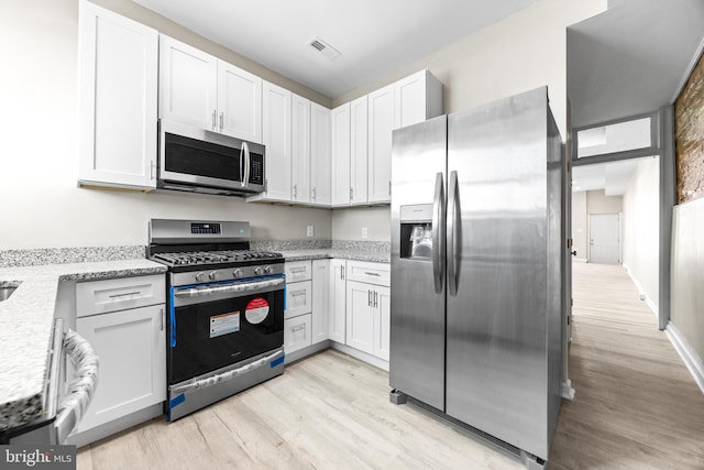 kitchen with light stone countertops, appliances with stainless steel finishes, light hardwood / wood-style floors, and white cabinetry