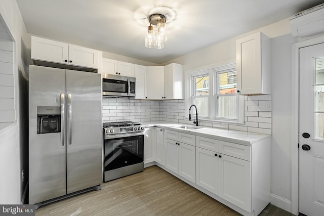 kitchen with sink, a wall unit AC, light hardwood / wood-style floors, white cabinets, and appliances with stainless steel finishes