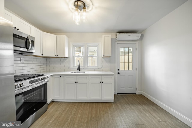 kitchen featuring a wall mounted air conditioner, sink, light hardwood / wood-style flooring, white cabinetry, and stainless steel appliances