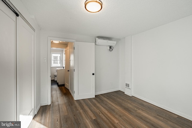 unfurnished bedroom featuring a textured ceiling, an AC wall unit, dark wood-type flooring, and a closet