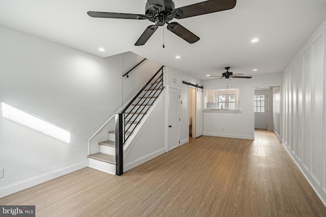 unfurnished living room with a barn door, ceiling fan, and light hardwood / wood-style floors