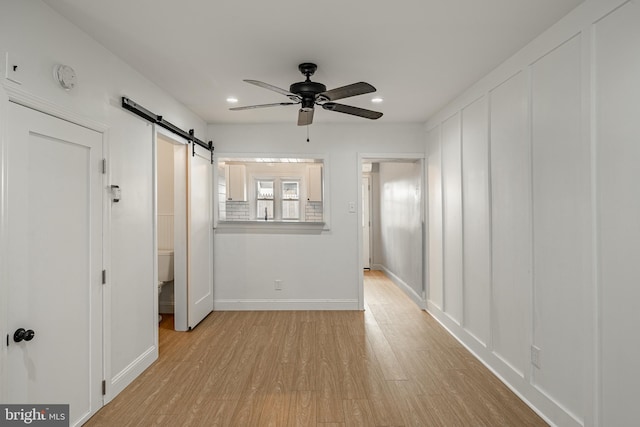 unfurnished room featuring a barn door, ceiling fan, and light hardwood / wood-style flooring