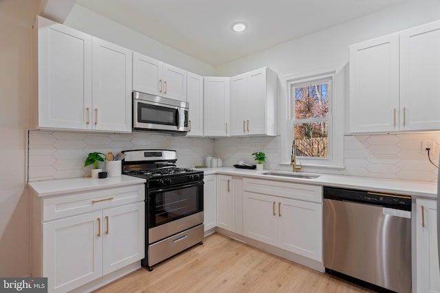 kitchen with sink, tasteful backsplash, light hardwood / wood-style floors, white cabinets, and appliances with stainless steel finishes