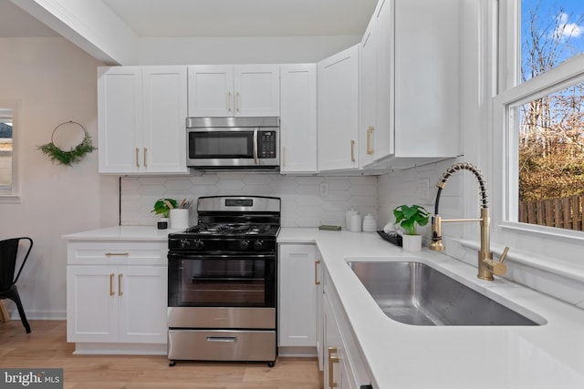 kitchen featuring appliances with stainless steel finishes, tasteful backsplash, sink, light hardwood / wood-style flooring, and white cabinetry