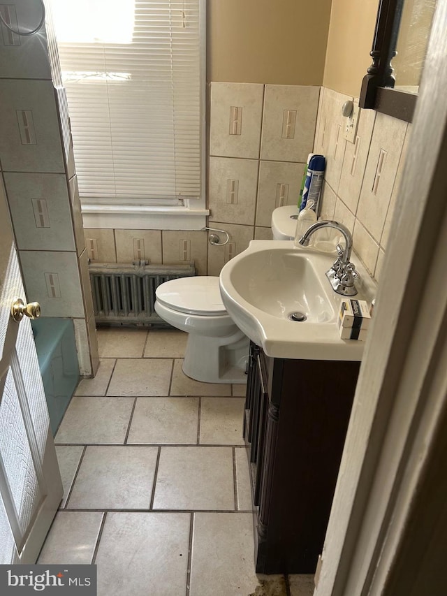 bathroom with vanity, radiator, a washtub, toilet, and tile walls