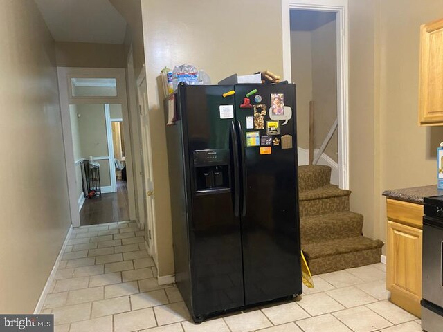 kitchen with black fridge with ice dispenser, light brown cabinets, stainless steel stove, and light tile patterned floors