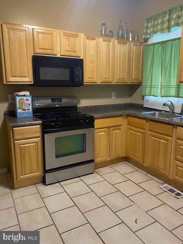 kitchen featuring light tile patterned floors, stainless steel gas range oven, and sink