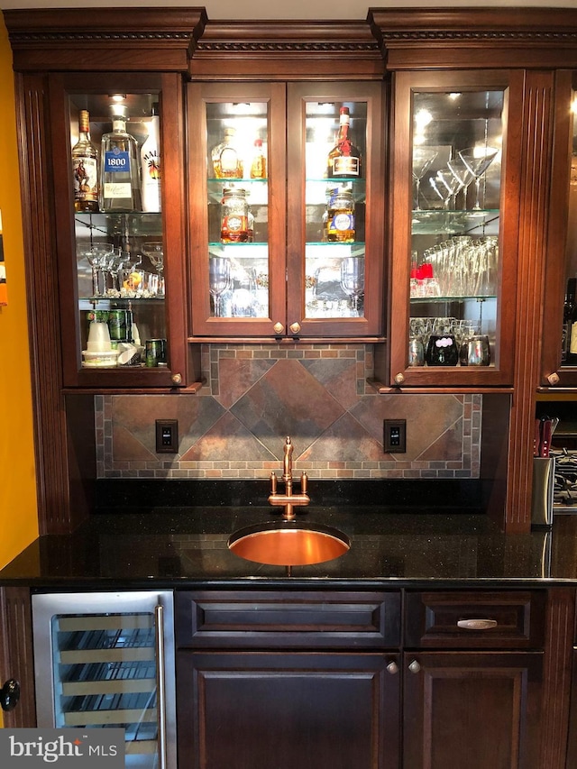 bar featuring decorative backsplash, beverage cooler, dark stone counters, and sink