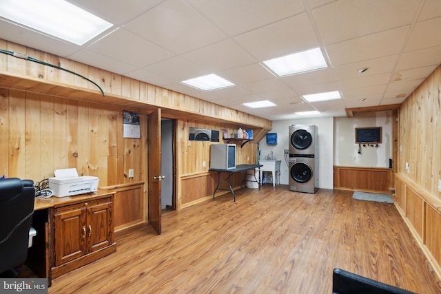 laundry area with wooden walls, sink, stacked washer and clothes dryer, and light wood-type flooring