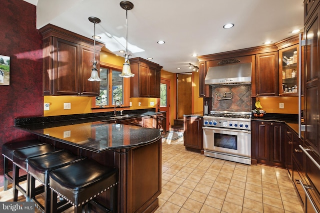 kitchen with sink, a kitchen breakfast bar, ventilation hood, high end stove, and decorative light fixtures