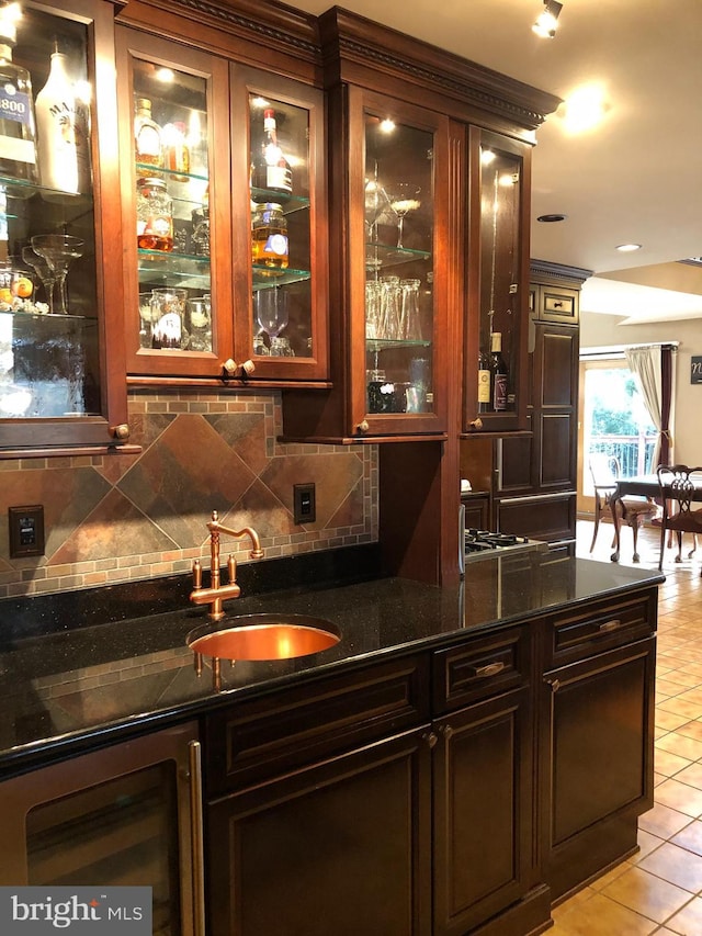 bar featuring light tile patterned flooring, dark brown cabinetry, dark stone counters, and sink