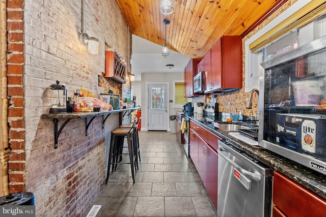 kitchen with backsplash, hanging light fixtures, brick wall, and appliances with stainless steel finishes