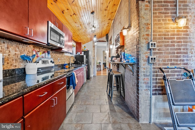 kitchen with pendant lighting, stainless steel appliances, brick wall, and tasteful backsplash