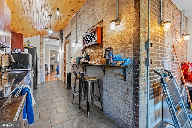 kitchen with sink, decorative light fixtures, wood ceiling, a breakfast bar area, and brick wall