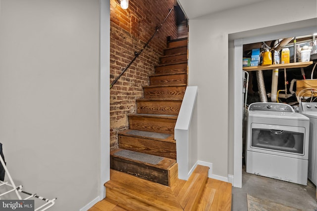 stairway with independent washer and dryer, hardwood / wood-style flooring, and brick wall